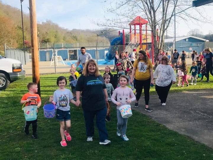 Children carrying baskets alongside church volunteers at an outdoor egg hunt