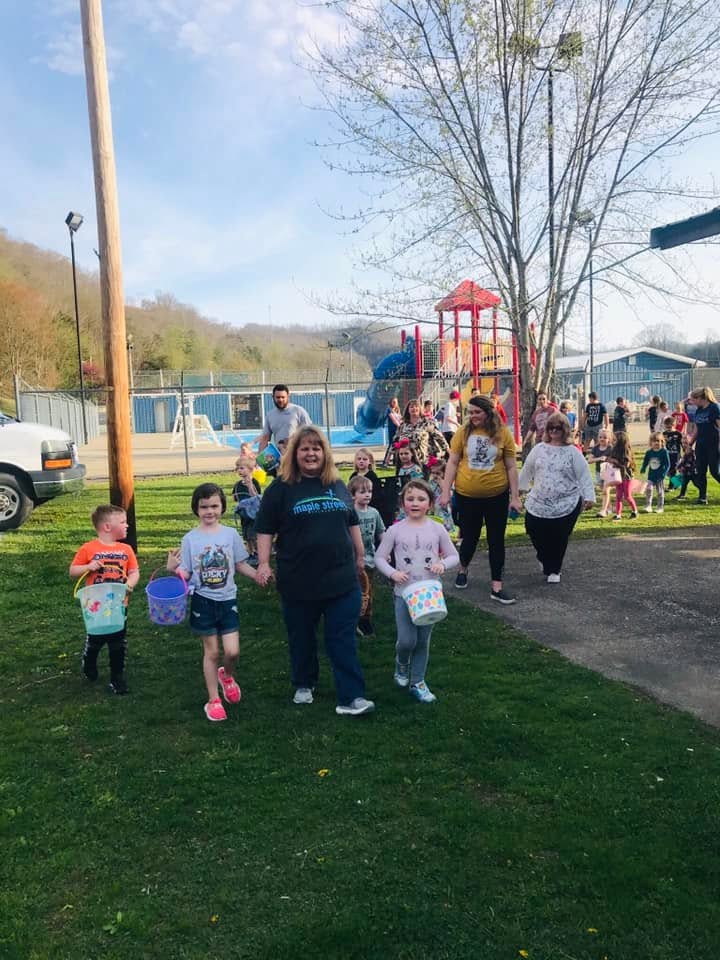 Children carrying baskets alongside church volunteers at an outdoor egg hunt