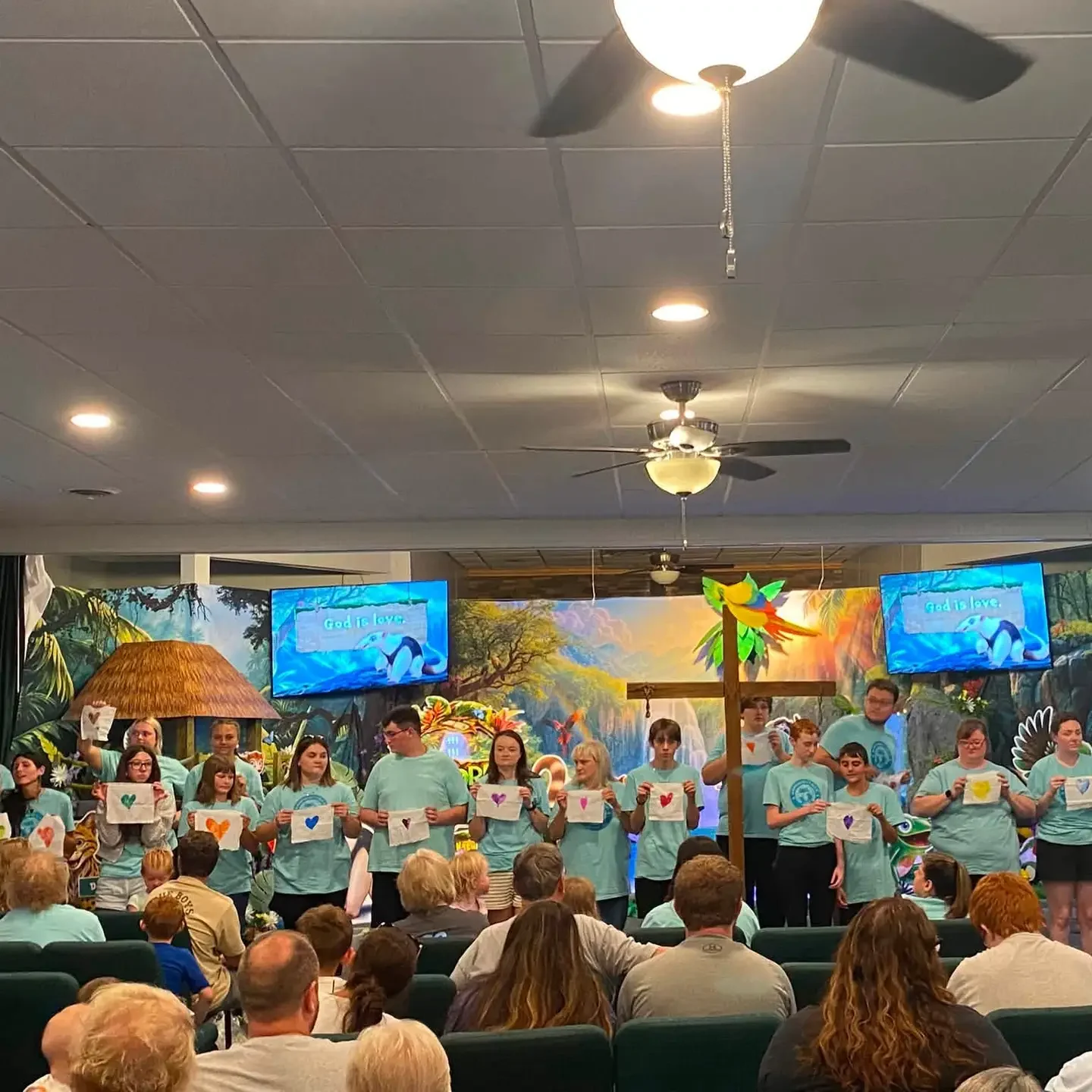 Children and leaders holding heart drawings during a Vacation Bible School presentation