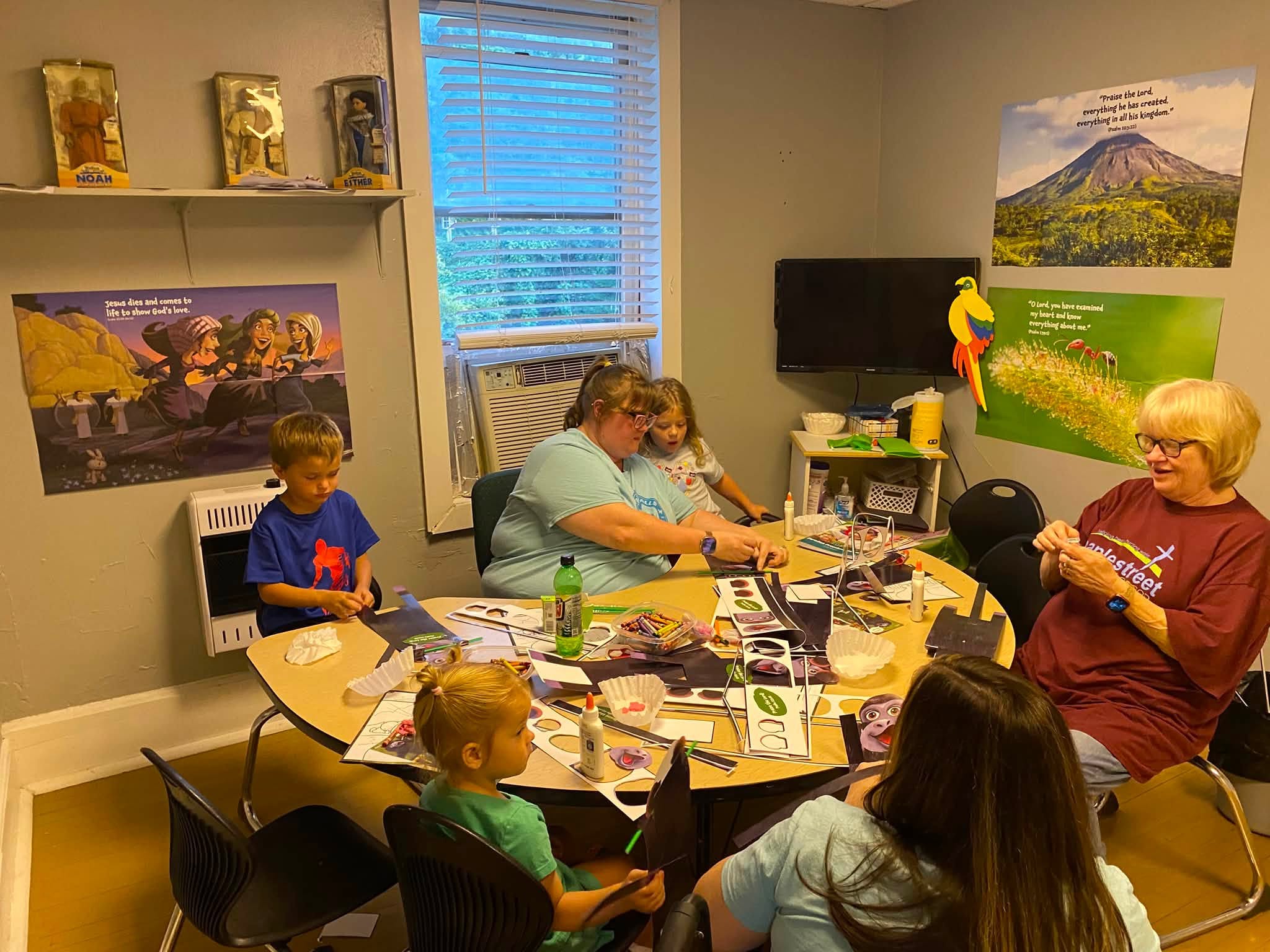 Children making crafts with VBS volunteers around a classroom table