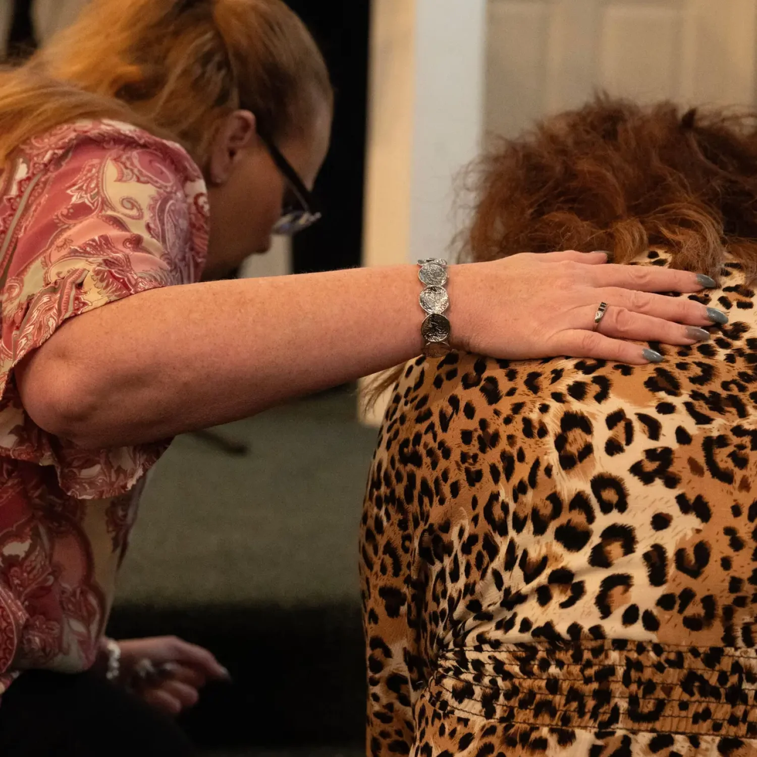 Two women praying together with a hand on a shoulder